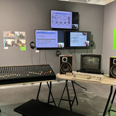Installation view of an exhibition, showing old equipment from a recording studio and three screens with demos of old music production software.